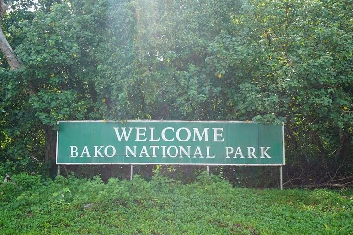 Ein großes grünes Willkommensschild für den Bako-Nationalpark, umgeben von Vegetation.